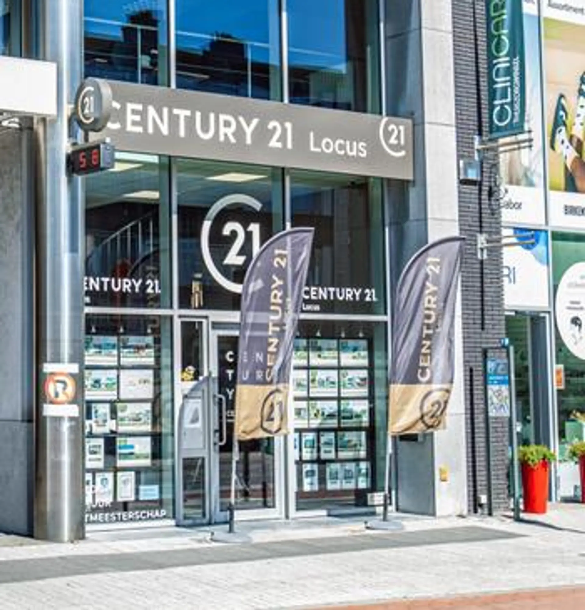 Voorgevel van het makelaarskantoor Century 21 Locus met vlaggen en etalageposters op straatniveau