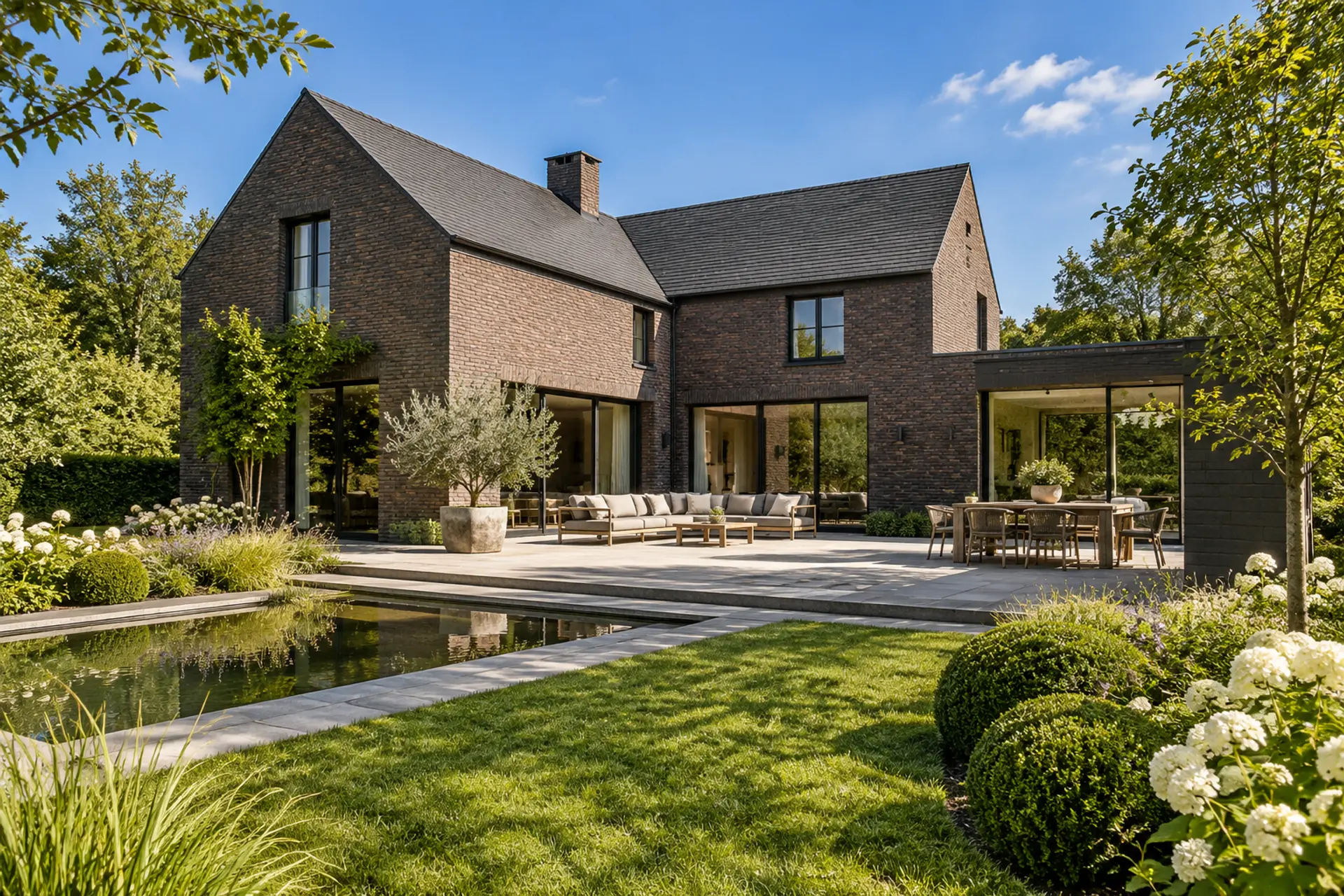 Villa in donkere baksteen met terras en groen onder blauwe lucht