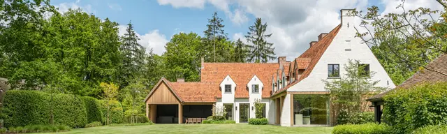 Witgeschilderde cottagevilla met oranje pannendak, houten carport en moderne glazen uitbouw in Brasschaat